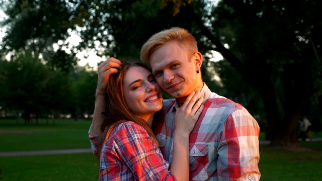 一个轻松的男人和他的女朋友站在一起抚摸她美丽的头发，拥抱她的肩膀，阳光明媚的公园和树木，夏天的幸福视频下载
