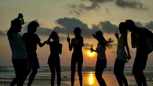 日落时分，一群年轻人在海滩聚会上跳舞的剪影。视频购买