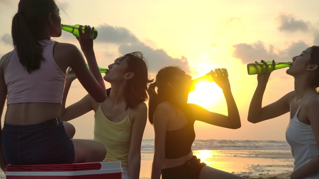一群女孩朋友有乐趣享受饮料和放松在海滩上日落。有聚会庆祝观念的人。慢动作镜头。视频购买