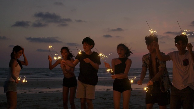 一群朋友在海边的夜晚聚会上玩的孟加拉灯在他们的手。青少年们在海滩上用烟花聚会。慢动作镜头。视频购买