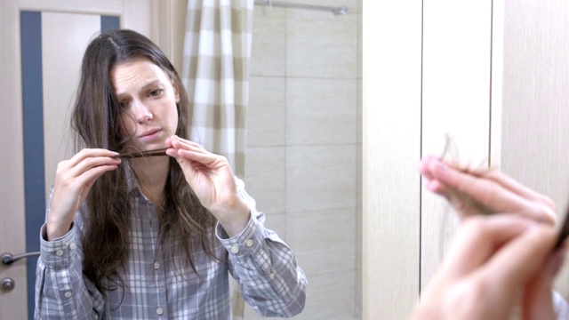 浴室里的女人看着自己干枯的头发。视频素材