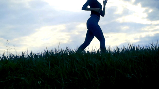 慢镜头特写，日出时女性奔跑的剪影背景。女孩慢跑的侧视图，跟踪拍摄在金色的日出近距离视频下载