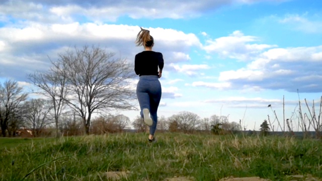一个年轻女子跑上长满青草的小山。慢动作跑步，慢跑慢动作，美丽的云朵，运动女性户外运动视频下载