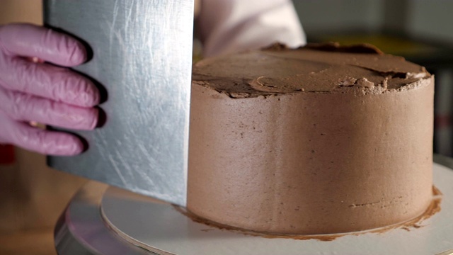 在面包店，糕点女厨师正用金属刮刀在旋转的蛋糕架上涂抹巧克力奶油。视频下载
