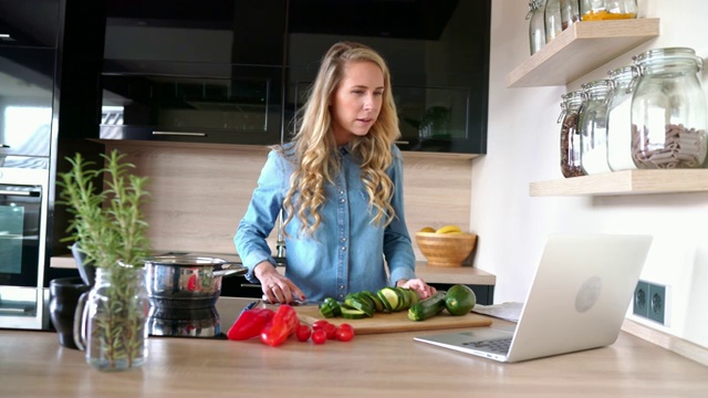 一个女人一边切菜一边在笔记本电脑上看菜谱视频素材