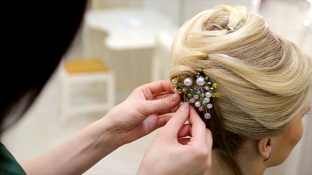 理发师把一个装饰品放在一个年轻的金发女人的头发上，特写视频素材