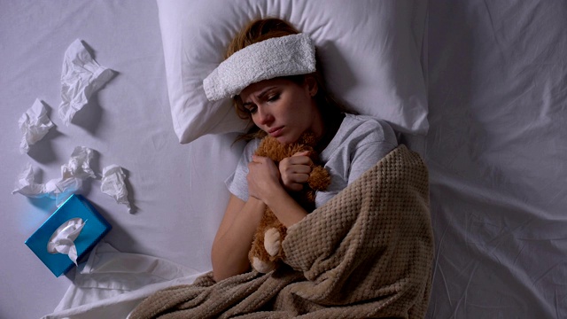 孤独的生病的女人抱着躺在床上的玩具熊和纸巾视频下载