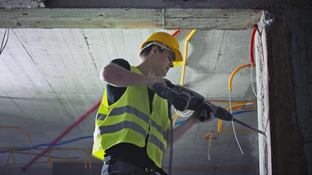 一名男性建筑工人正在用手提钻在墙上挖一个洞来装管子视频素材