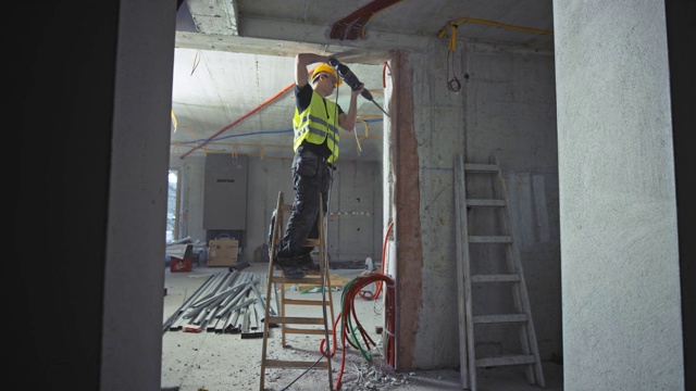 男建筑工人站在建筑物内的梯子上使用手提钻视频下载