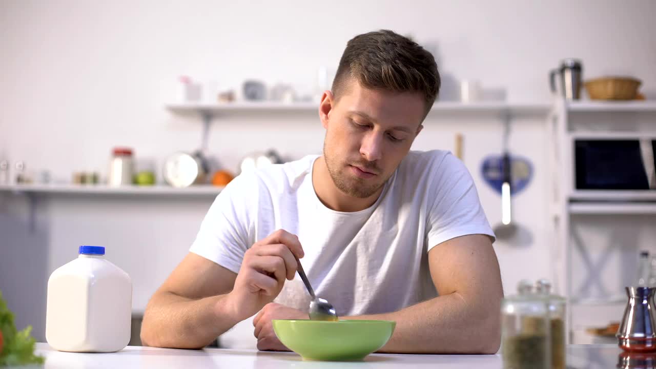 心烦的单身男子早餐吃无味的麦片，食欲不振视频下载