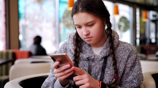 一个少女坐在咖啡馆用智能手机发短信。视频素材