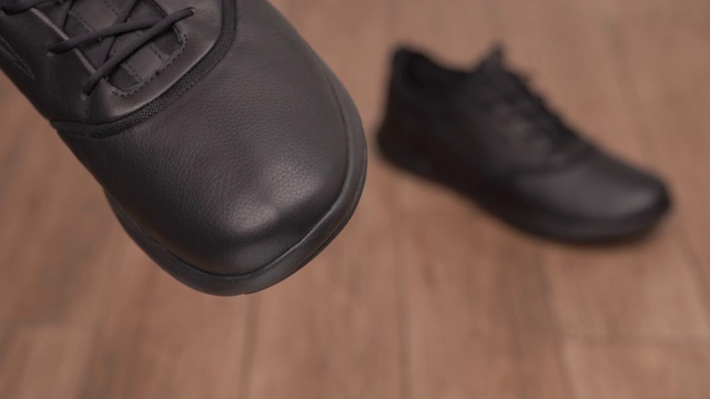 一个男性手握和清洁黑色皮鞋的特写在前景。休闲风格的干净鞋上模糊的背景。视频素材