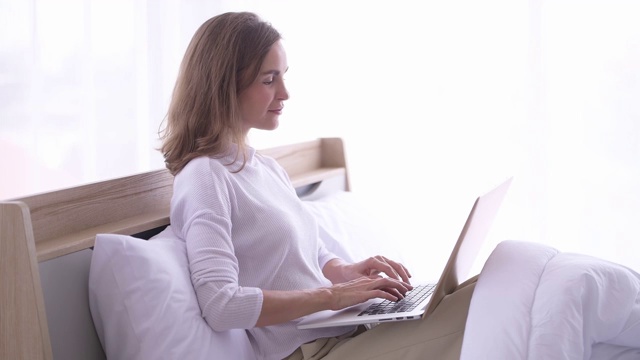 女商人在卧室里用笔记本电脑工作。用信用卡在网上购物的女人视频素材