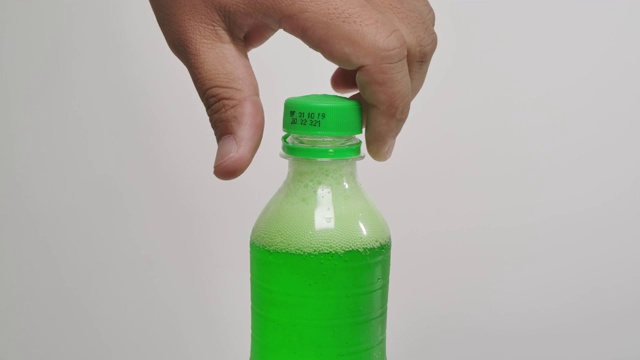 一个男人打开绿色气泡软饮料的瓶盖在白色的背景上的特写。视频下载
