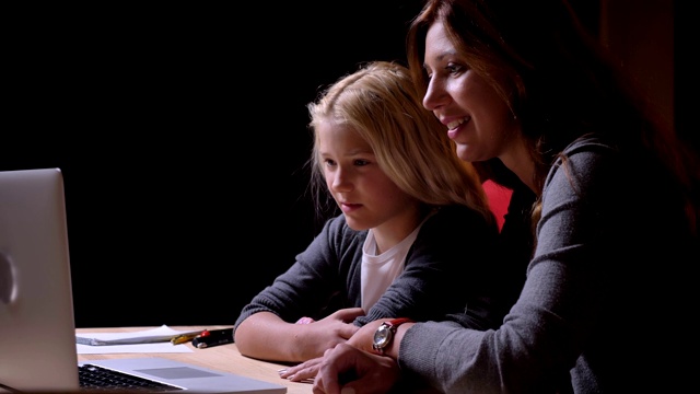 年轻的白人母亲和她的小女孩看电影的特写，在笔记本电脑和笑视频下载