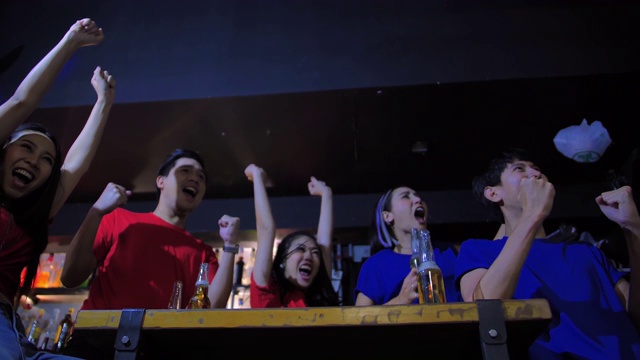 不同的亚洲朋友群在体育酒吧看电视。他们队进了一球，赢了。兴奋的朋友一边看足球比赛一边在酒吧喝啤酒。当他们喜欢的球队得分时，他们都欢呼。快乐的年轻人。视频下载