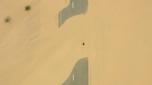 从空中俯瞰，一个身份不明的人走在迪拜沙漠中被沙丘覆盖的荒芜道路上。阿拉伯联合酋长国迪拜。视频下载