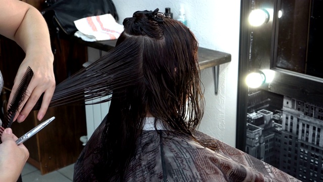 女孩在理发店剪头发。她坐在镜子前，女发型师用剪刀剪她的发梢。关闭了。4 k。视频素材
