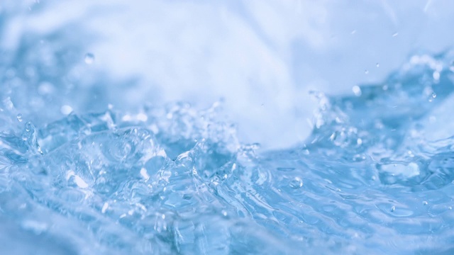 三个冰块落入旋转的浅蓝色的水中，溅起水花和泡泡，特写慢镜头。视频购买