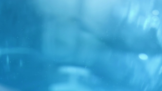 水滴在蓝色色调的水面上形成涟漪，在近距离和缓慢的运动视频购买