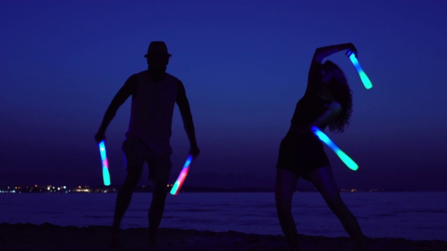 年轻的夫妇在晚上拿着发光的棍子跳舞视频下载