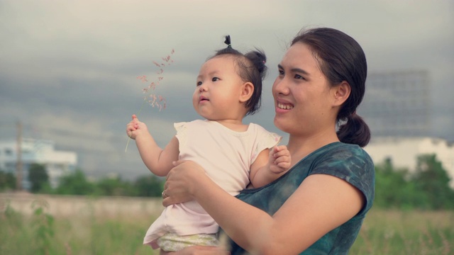 亚洲年轻的母亲和女儿在草地上日落。幸福的家庭的概念。实时手持拍摄。4 k视频素材