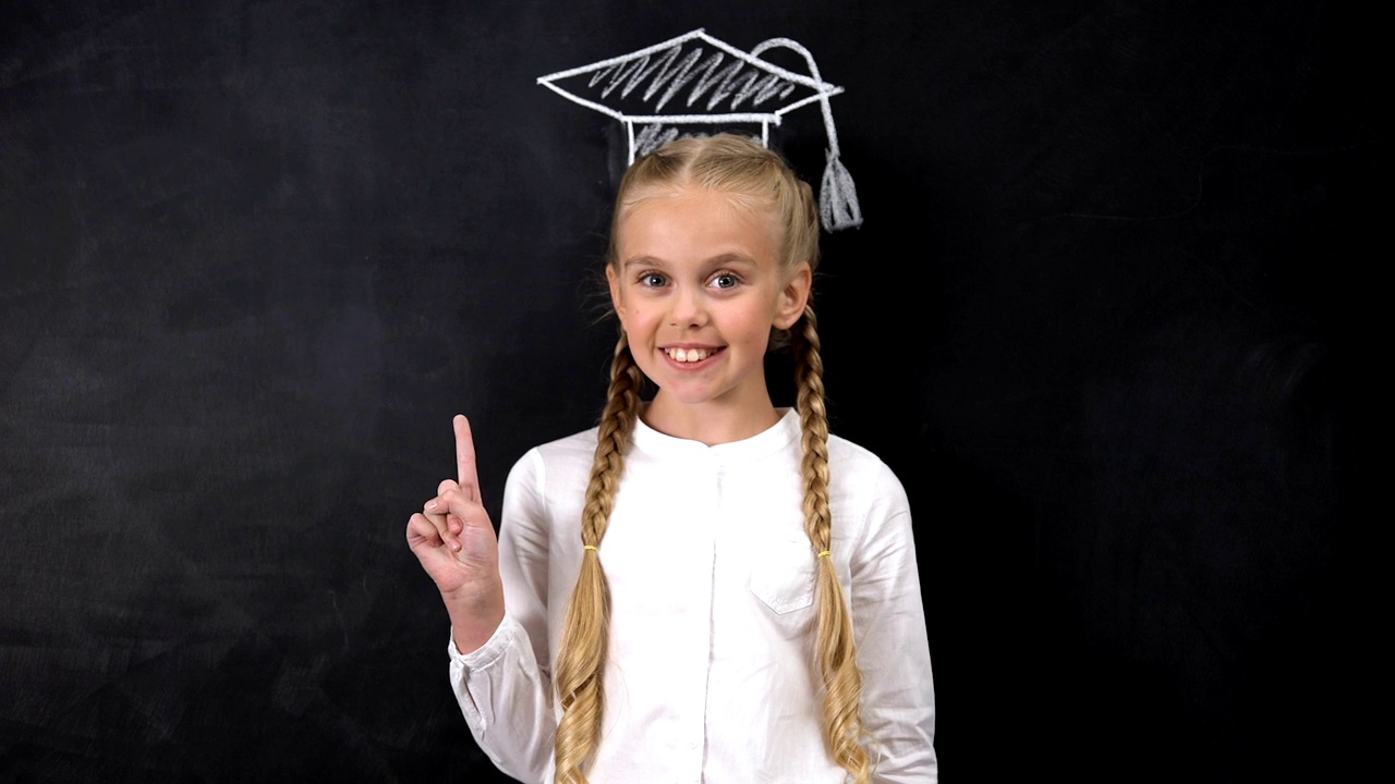 快乐的女生指着黑板背景上的学帽视频下载