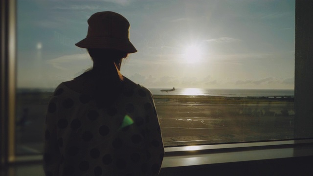 年轻的亚洲女子站在机场的窗口，观察日落的飞机视频下载
