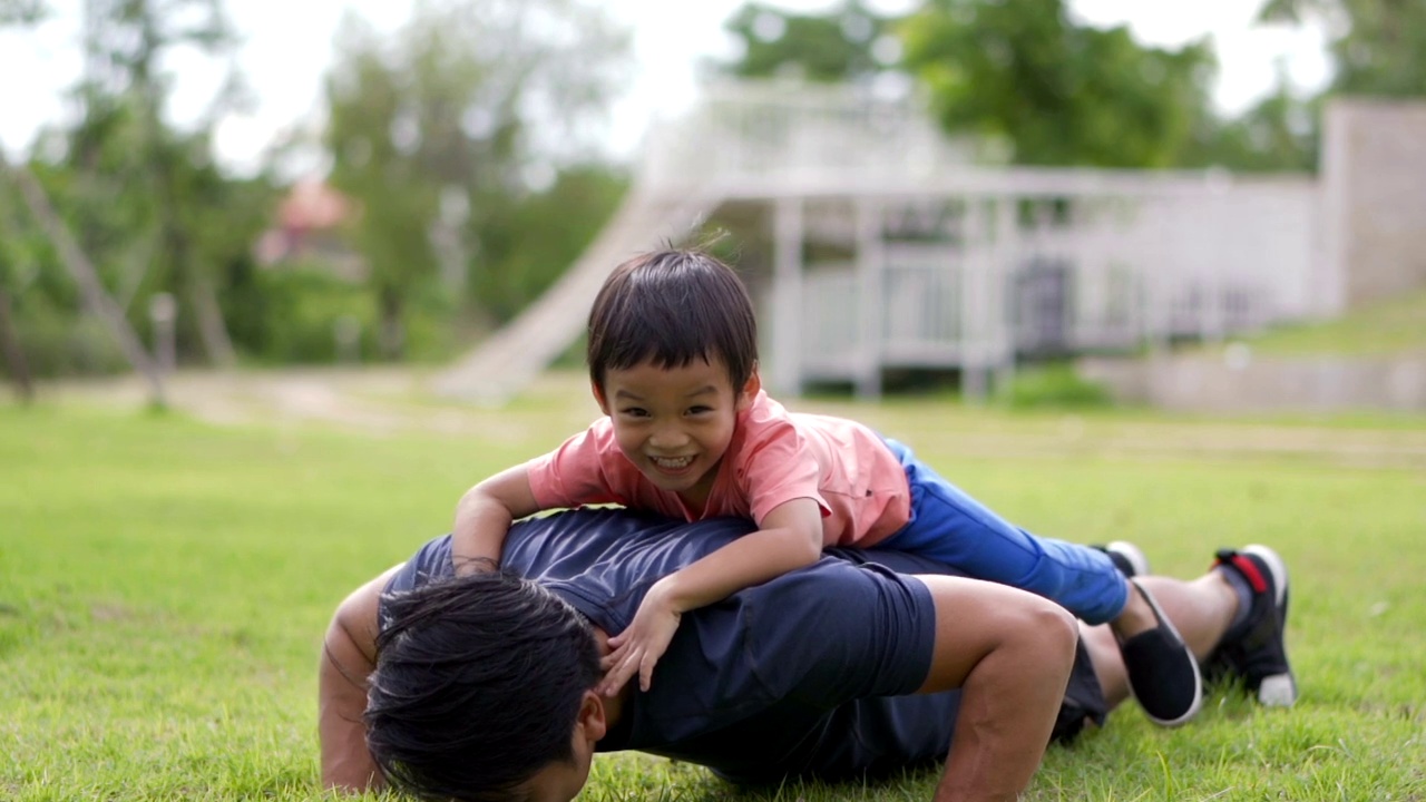 亚洲父亲在户外做俯卧撑，让小男孩躺在他的背上。视频下载