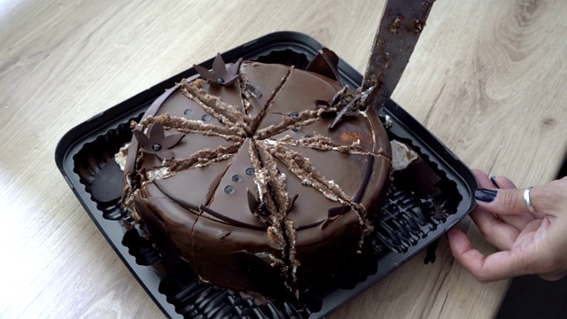 女人把巧克力蛋糕切成大块，上面装饰着巧克力花。蛋糕放在厨房桌子上的礼品盒里。关闭了。从上往下看。4 k。视频下载