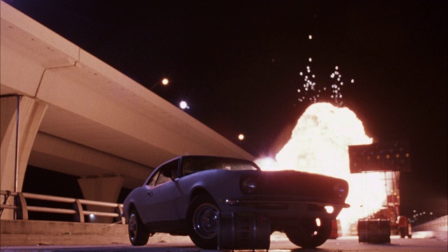 中等角度的灰色福特野马老爷车停在高速公路匝道上。见黄色箭头。汽车爆炸，一个火球，火焰和烟雾从窗户中滚滚而出。爆炸。视频购买