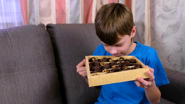 男孩坐在沙发上闻着盒子里的巧克力。视频素材