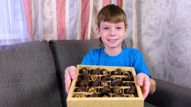 男孩坐在沙发上展示盒子里的巧克力。视频下载