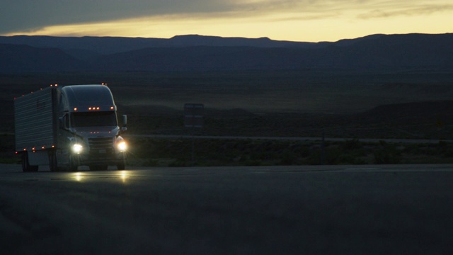 黃昏時分，一輛開著前燈的半掛卡車在科羅拉多西部的高沙漠中行駛視頻素材