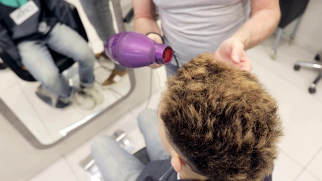 高角度拍摄一名年轻男子的理发师正在烘干头发视频下载
