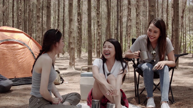 一群年轻的亚洲朋友一起在森林里露营或野餐，十几岁的女性喜欢在帐篷前聊天。女人在夏天的假期里做冒险活动和旅游。缓慢的运动。视频购买