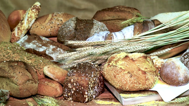 特写在桌子上新鲜的糕点与小麦穗在一个轻的织物背景。各种面包的特写镜头。视频下载