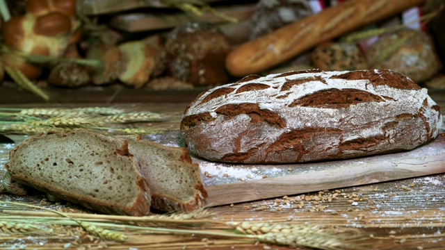 两片硬皮面包和一整条面包放在桌子上，背景是其他各种各样的面包。视频素材
