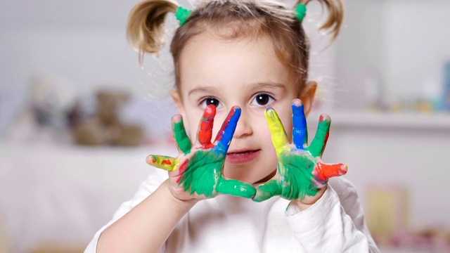 一个小女孩的肖像，在她的卧室里，显示她的双手都是彩色的。视频素材