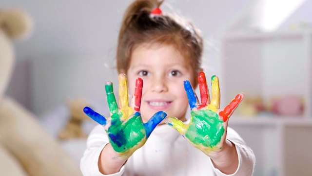 一个小女孩的肖像，在她的卧室里，显示她的双手都是彩色的。视频素材