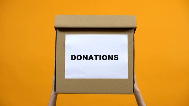 手握捐款箱，橙色背景，人道主义援助，利他主义视频下载