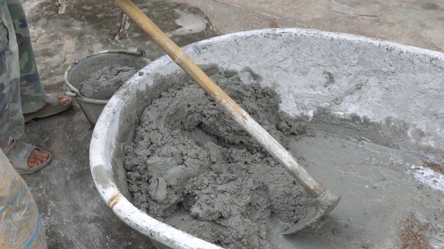 工人在托盘中搅拌用于施工的水泥。建筑工人把水和沙子放在混凝土上搅拌水泥视频下载
