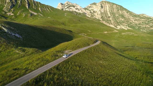 鳥瞰圖的白色汽車行駛在山區蜿蜒的道路在日落的燈光。航拍4K無人機拍攝視頻素材
