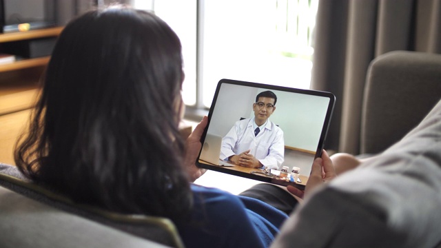 亞洲年輕女子躺在沙發上，用平板電腦與醫生進行視頻會議視頻素材