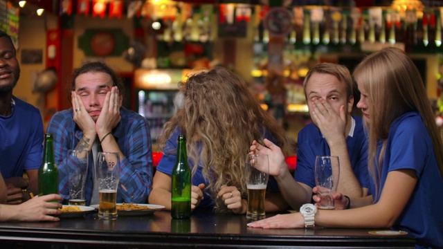 啤酒吧里穿着蓝色t恤的情绪激动的球迷。多种族的非洲裔美国人因为他们团队的失败而感到沮丧和悲伤。视频素材
