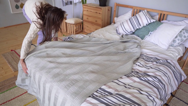 一个穿家居服的女人下了床，用灰色格子布铺床。Loft斯堪的纳维亚式公寓视频素材