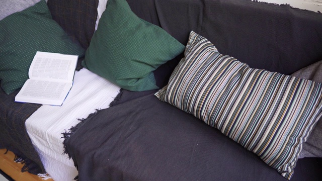 Hygge概念。带有暖色枕头和毯子的沙发，一本书和一个格子图案的特写。视频素材