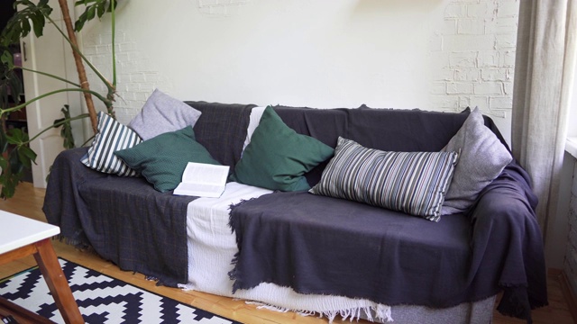 柔软漂亮舒适的沙发上有一本书，枕头，格子和毯子。Lagom概念视频素材