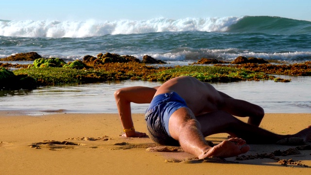 穿着短裤的壮汉坐在潮湿的黄沙上舒展着身体视频下载