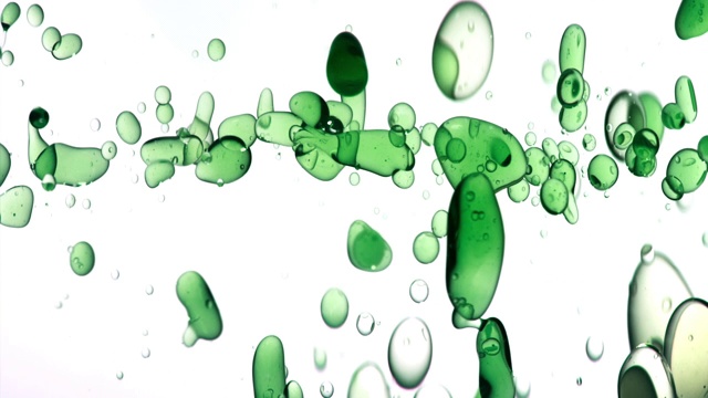 近距离和缓慢的运动倒绿色的油从右边和创造一排泡沫水下，而弹跳在白色的背景视频素材
